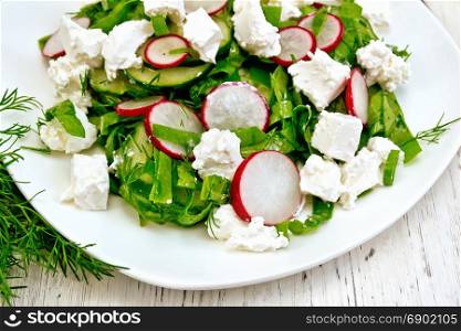 Salad with spinach, cucumbers, radish and salted cheese, dill and green onion in a plate on the background of a wooden board