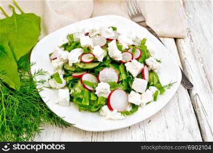 Salad with spinach, cucumbers, radish and salted cheese, dill and green onions in a plate, a towel on the background of a wooden board
