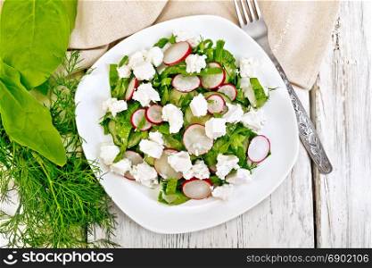 Salad with spinach, cucumbers, radish and salted cheese, dill and green onions in a bowl, towel on the background of a wooden board from above