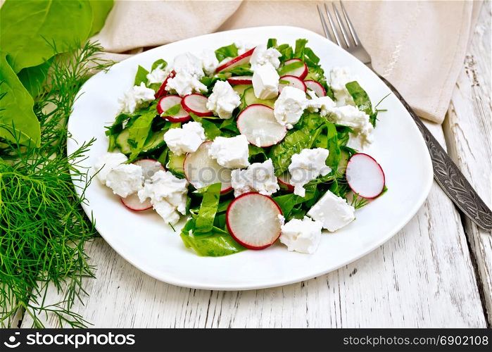 Salad with spinach, cucumbers, radish and salted cheese, dill and green onions in a white plate, a towel on the background of a wooden board