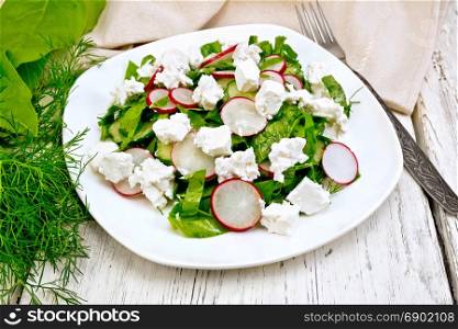 Salad with spinach, cucumbers, radish and salted cheese, dill and green onions in a white plate, a towel on the background of a wooden board