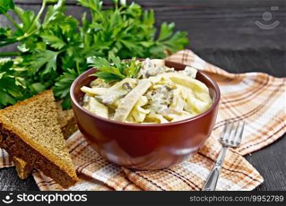 Salad with squid, egg and mushrooms in a bowl on a napkin, bread, a fork and parsley on wooden board background