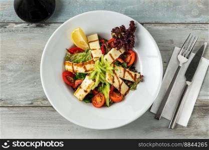 Salad with tomato and halloumi cheese on wooden table