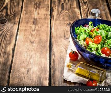 Salad with tomatoes and fresh greens with olive oil. On a wooden table. Salad with tomatoes and greens