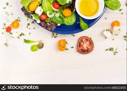 Salad with tomatoes, feta cheese and oil vinegar in blue plate on white wooden background, top view frame
