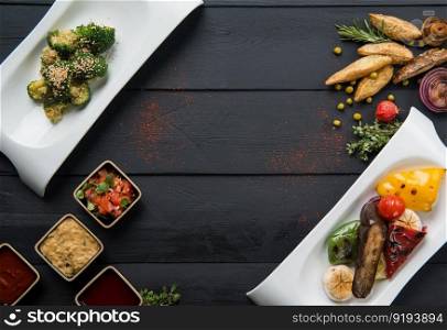 salads, vegetable food and gravy in plates on a black wooden background. the food, the view from the top