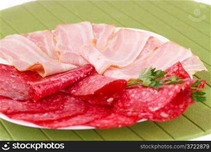 Salami and bacon on plate isolated on green background.
