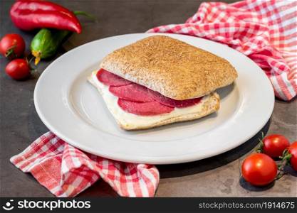 Salami and cheddar sandwich on white porcelain plate on stone table