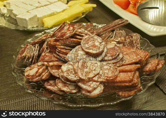 Salami and sausages sliced and arranged in plate closeup at table with other appetizers