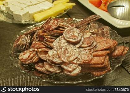 Salami and sausages sliced and arranged in plate closeup at table with other appetizers