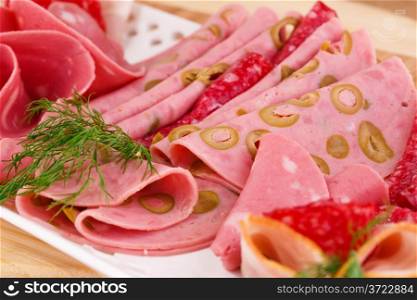 Salami, mortadella and bacon on plate on wooden board.