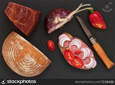 Salami, sauce, with peppers and onions. View from above. Black stone background.
