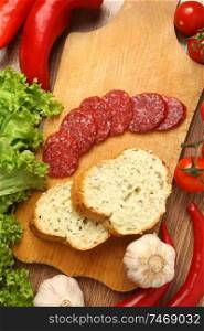 Salami sausage on a cutting board surrounded with various vegetables