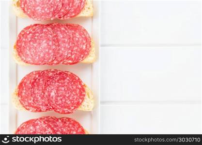 Salami slices on ciabatta bread, photographed overhead on white wood (Selective Focus, Focus on the salami slices). Salami Sandwich