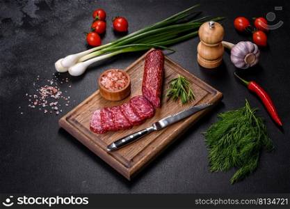 Salami with fresh rosemary and sπces. On a black sto≠background. Smoked salami with rosemary, garlic and tomatoes on wooden cutting board