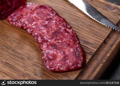 Salami with fresh rosemary and spices. On a black stone background. Smoked salami with rosemary, garlic and tomatoes on wooden cutting board
