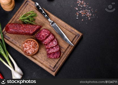 Salami with fresh rosemary and spices. On a black stone background. Smoked salami with rosemary, garlic and tomatoes on wooden cutting board