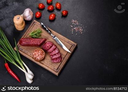 Salami with fresh rosemary and spices. On a black stone background. Smoked salami with rosemary, garlic and tomatoes on wooden cutting board