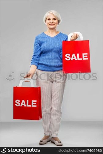 sale and old people concept - smiling senior woman with red shopping bags over grey background. senior woman with sale word on red shopping bags