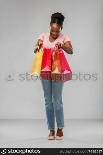 sale and people concept - happy smiling african american young woman with shopping bags over grey background. happy african american woman with shopping bags