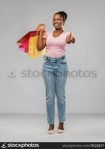 sale and people concept - happy smiling african american young woman with shopping bags showing thumbs up over grey background. happy african american woman with shopping bags