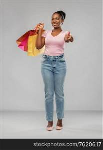 sale and people concept - happy smiling african american young woman with shopping bags showing thumbs up over grey background. happy african american woman with shopping bags