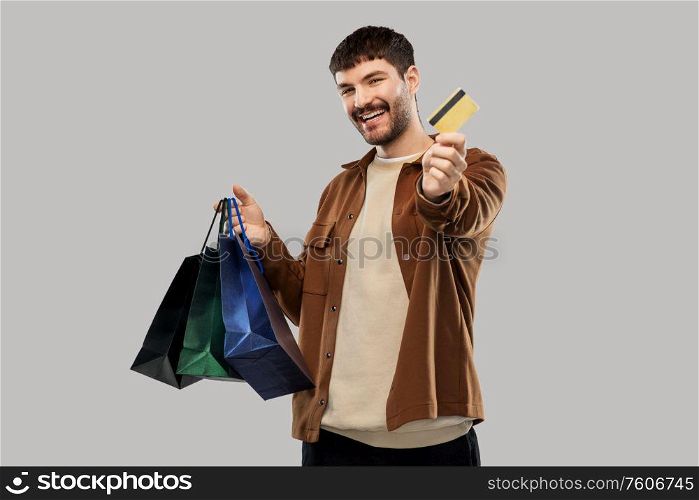 sale and people concept - happy smiling young man with shopping bags and credit card over grey background. happy young man with shopping bags and credit card