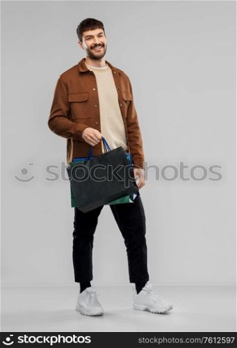 sale and people concept - happy smiling young man with shopping bags over grey background. happy smiling young man with shopping bags