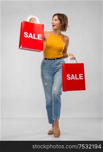 sale and people concept - happy smiling young woman in mustard yellow top and jeans with shopping bags over grey background. happy smiling young woman with shopping bags