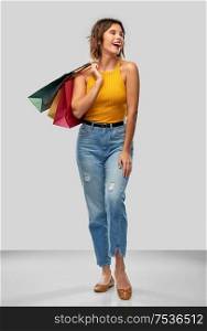 sale and people concept - happy smiling young woman in mustard yellow top and jeans with shopping bags over grey background. happy smiling young woman with shopping bags