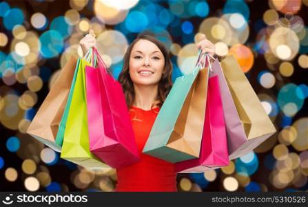 sale and people concept - smiling woman with colorful shopping bags over holidays lights background. happy woman with colorful shopping bags