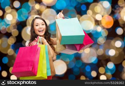 sale and people concept - smiling woman with colorful shopping bags over holidays lights background. happy woman with colorful shopping bags