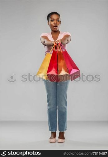 sale and people concept - surprised african american young woman with shopping bags over grey background. african american woman with shopping bags