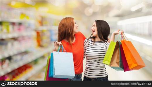 sale and people concept - two smiling teenage girls with shopping bags over supermarket background. teenage girls with shopping bags and credit card