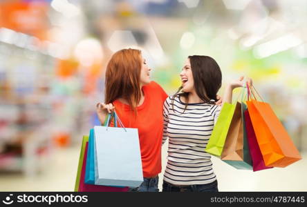 sale and people concept - two smiling teenage girls with shopping bags over supermarket background. teenage girls with shopping bags and credit card