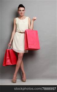 Sale and retail concept. Fashion woman girl in full length wearing elegant white dress with red shopping bags in hands, grey background studio shot.