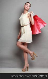 Sale and retail. Young woman girl in full length in elegant white dress with red shopping bags on grey background in studio.