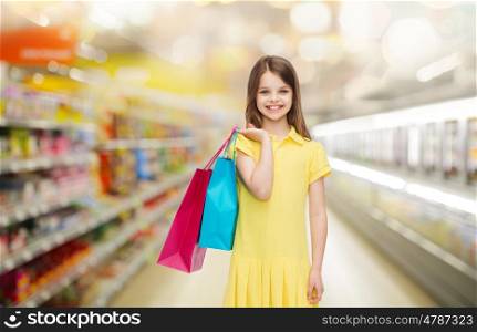 sale, children and people concept - smiling little girl in yellow dress with shopping bags over supermarket background