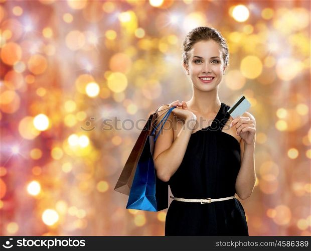sale, christmas and holidays concept - smiling woman in dress with shopping bags and credit card over lights background
