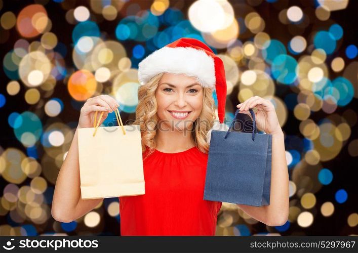 sale, christmas, holidays and people concept - smiling woman in santa hat with shopping bags over lights background. woman in santa hat with christmas shopping bags