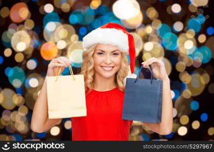 sale, christmas, holidays and people concept - smiling woman in santa hat with shopping bags over lights background. woman in santa hat with christmas shopping bags