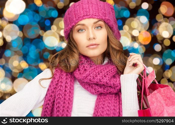 sale, christmas, holidays and people concept - smiling woman in winter hat with shopping bags over lights background. woman in winter hat with christmas shopping bags