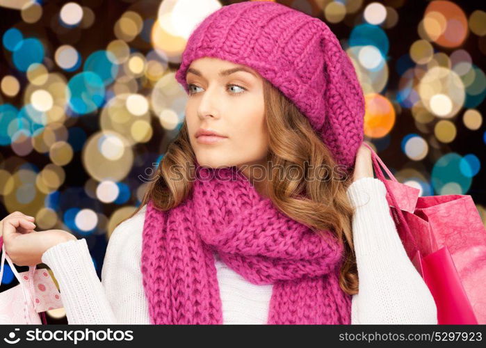 sale, christmas, holidays and people concept - smiling woman in winter hat with shopping bags over lights background. woman in winter hat with christmas shopping bags