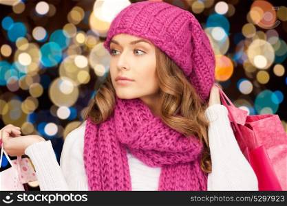 sale, christmas, holidays and people concept - smiling woman in winter hat with shopping bags over lights background. woman in winter hat with christmas shopping bags