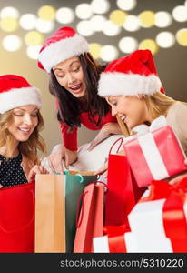 sale, christmas, holidays and people concept - smiling women in santa helper hats with shopping bags and many gift boxes over lights background. women with shopping bags and christmas gifts