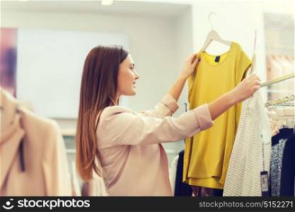 sale, clothes , shopping, fashion and people concept - happy young woman choosing between two shirts in mall or clothing store. happy young woman choosing clothes in mall