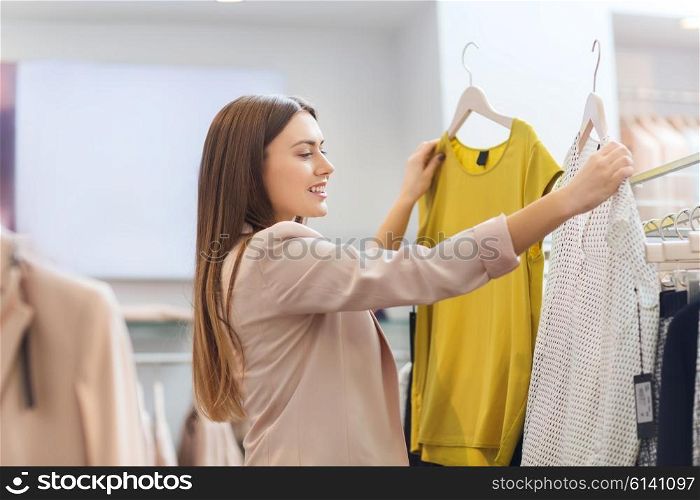 sale, clothes , shopping, fashion and people concept - happy young woman choosing between two shirts in mall or clothing store