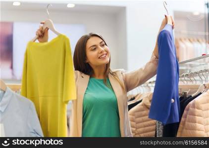 sale, clothes , shopping, fashion and people concept - happy young woman choosing between shirt and jacket at clothing store