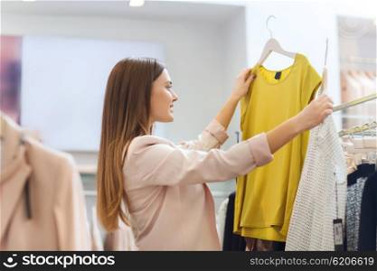 sale, clothes , shopping, fashion and people concept - happy young woman choosing between two shirts in mall or clothing store
