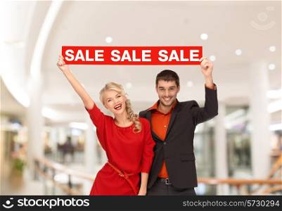 sale, consumerism, advertisement and people concept - happy young couple holding red advertising board in mall